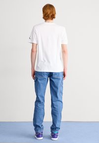 Camiseta de algodón blanca, de mangas cortas y con escote redondo, combinada con unos vaqueros de mezclilla azul claro y zapatillas con acentos morados.
