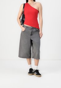 Rode top met één schouder, grijze wijde denim shorts, zwarte sneakers met witte strepen en witte sokken. Zwarte handtas met schouderriem.