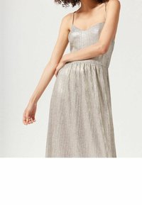 Skinande silverklänning med tunna axelband, en hjärtformad halsringning och en plisserad kjol, gjord av textil med metallisk struktur.