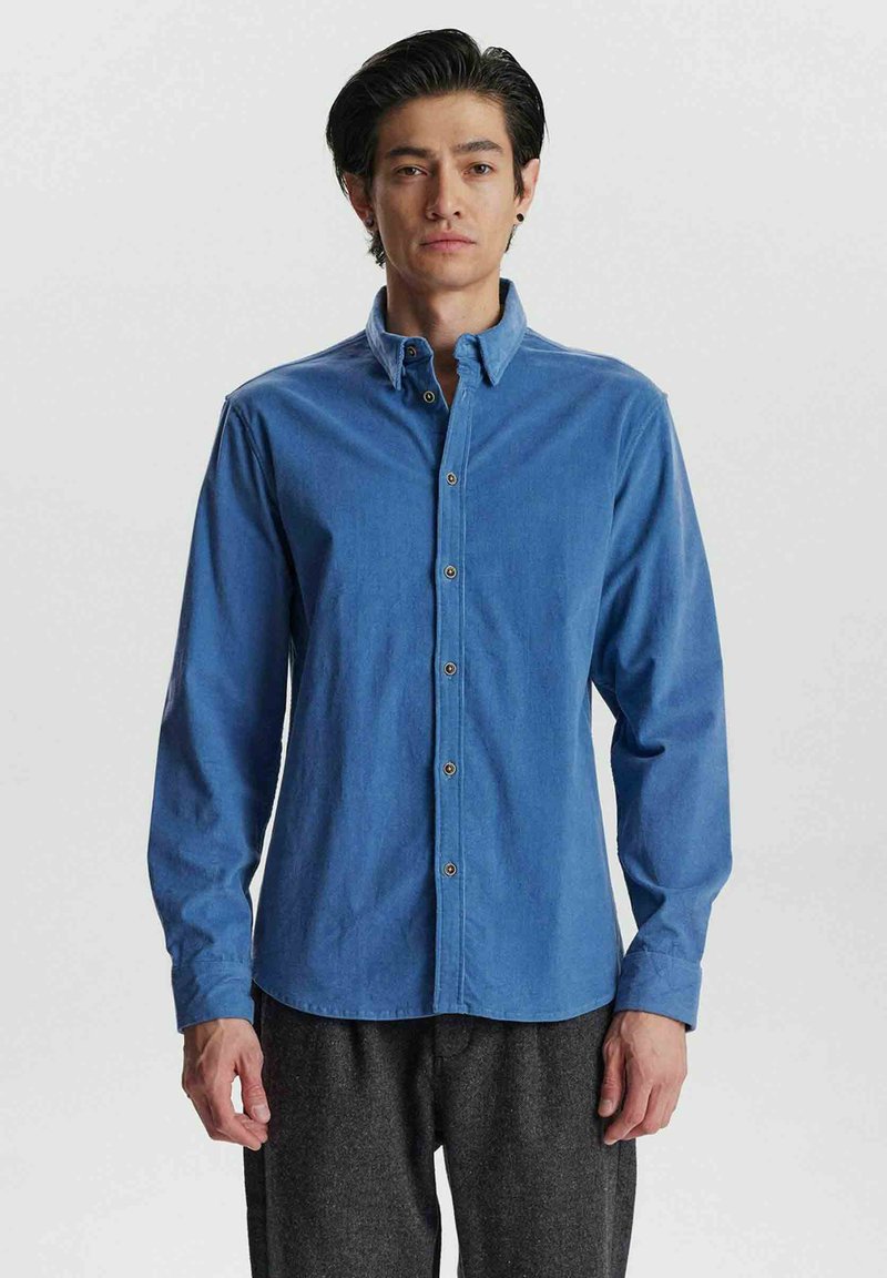 Camisa azul de botones hecha de una mezcla de algodón, con mangas largas, un cuello clásico y botones marrones en la tapeta delantera.