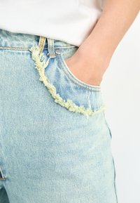Light blue denim shorts with frayed edges and a raw hem. Features a classic five-pocket design and contrast stitching.