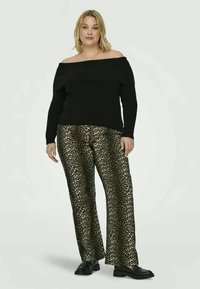 Suéter preto sem ombros combinado com calças largas com padrão de leopardo em dourado e preto, usadas com sapatos planos pretos.