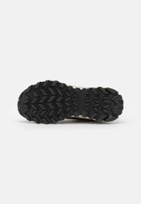 Suela de zapatilla para correr por senderos con una base de goma negra y patrones de suela agresivos para tracción, y elementos de diseño sutiles en tonos más claros.