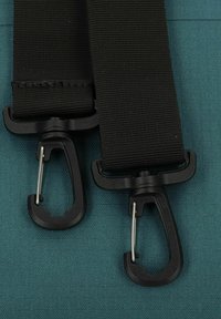 Cinghie in nylon nero con finitura opaca, dotate di ganci in plastica e accenti metallici, appoggiate su uno sfondo testurizzato color teal.