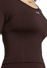 Brown athletic top made of smooth fabric, featuring a ribbed texture on the sides and a white logo on the chest. Round neckline.