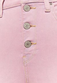 Gros plan sur un tissu en denim rose avec trois boutons métalliques et des surpiqûres jaunes le long du bord et des passants de ceinture.