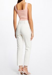 Top in maglia rosa aderente con schiena quadrata, abbinato a pantaloni bianchi sartoriali. I pantaloni presentano una trama liscia e una vita elasticizzata. Tacchi a spillo bianchi con cinturini.