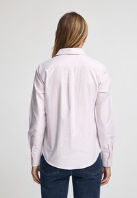 Ljust rosa skjorta med knappar och tunna vita ränder, med klassisk krage, långa ärmar och rundad nederdel. Tyget verkar slätt.