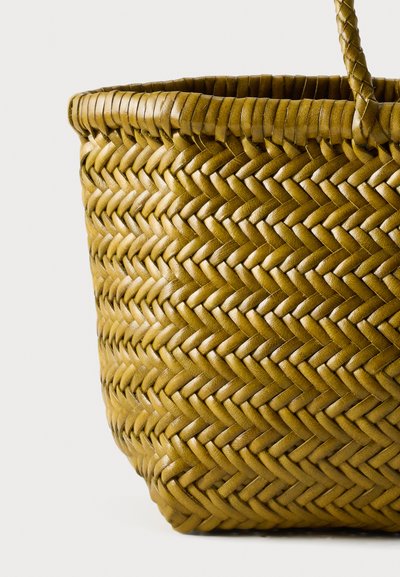 Καφέ υφαντό δερμάτινο καλάθι με πλεχτή λαβή και περίπλοκο σχέδιο ψαροκόκκαλου σε απλό ανοιχτό φόντο.