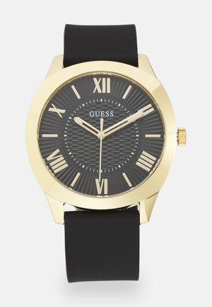 Fekete óra kerek, arany színű házzal, érdessé tett fekete számlappal, római számjegyekkel és fekete gumi szíjjal. Arany díszítések a mutatókon.