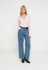 Ροζ ανοιχτόχρωμο μπλουζάκι με μακριά μανίκια και V-λαιμόκοψη, συνδυασμένο με ψηλόμεσα μπλε τζιν παντελόνια φαρδιάς γραμμής και μαύρη ζώνη. Μαύρα μποτάκια μέχρι τον αστράγαλο ολοκληρώνουν την εμφάνιση.