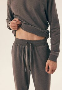 Szara bluzka z długim rękawem oraz dopasowane dresy z elastycznym pasem i sznurkiem. Tkanina wydaje się być miękka i teksturowana.