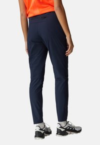 Pantalon de sport bleu marine ajusté, avec une taille élastique et une poche zippée. Associé à des chaussures de sport blanches et noires.