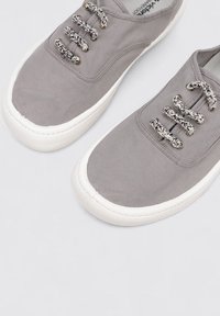 Sneakers in tela grigia con suole in gomma bianca, punta tonda e lacci intrecciati. Presentano una texture liscia e un design minimalista.