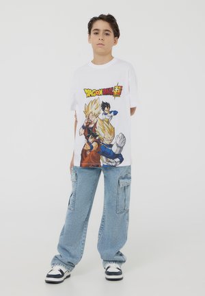 T-shirt bianco in cotone con grafica colorata di Dragon Ball Super e personaggi. Abbinato a pantaloni cargo leggeri blu chiaro e sneakers.