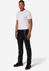 Zwarte leren broek met zijsluitingen, gecombineerd met een aansluitend wit T-shirt. De laarzen hebben een dikke zool en een vetersluiting.