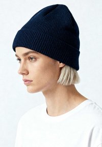 Cappellino a maglia blu navy con trama a coste e dettaglio cuciture, aderente alla testa, abbinato a una maglietta bianca semplice.