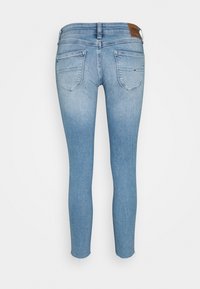 Světle modré skinny džíny s dvěma zadními kapsami, neupraveným lemem a hnědou koženou nášivkou značky na pásku na bílém pozadí.