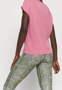 Rosa t-shirt med kort ärm har en avslappnad passform och mjuk textur, med gröna leggings i leopardmönster och svarta sidor.