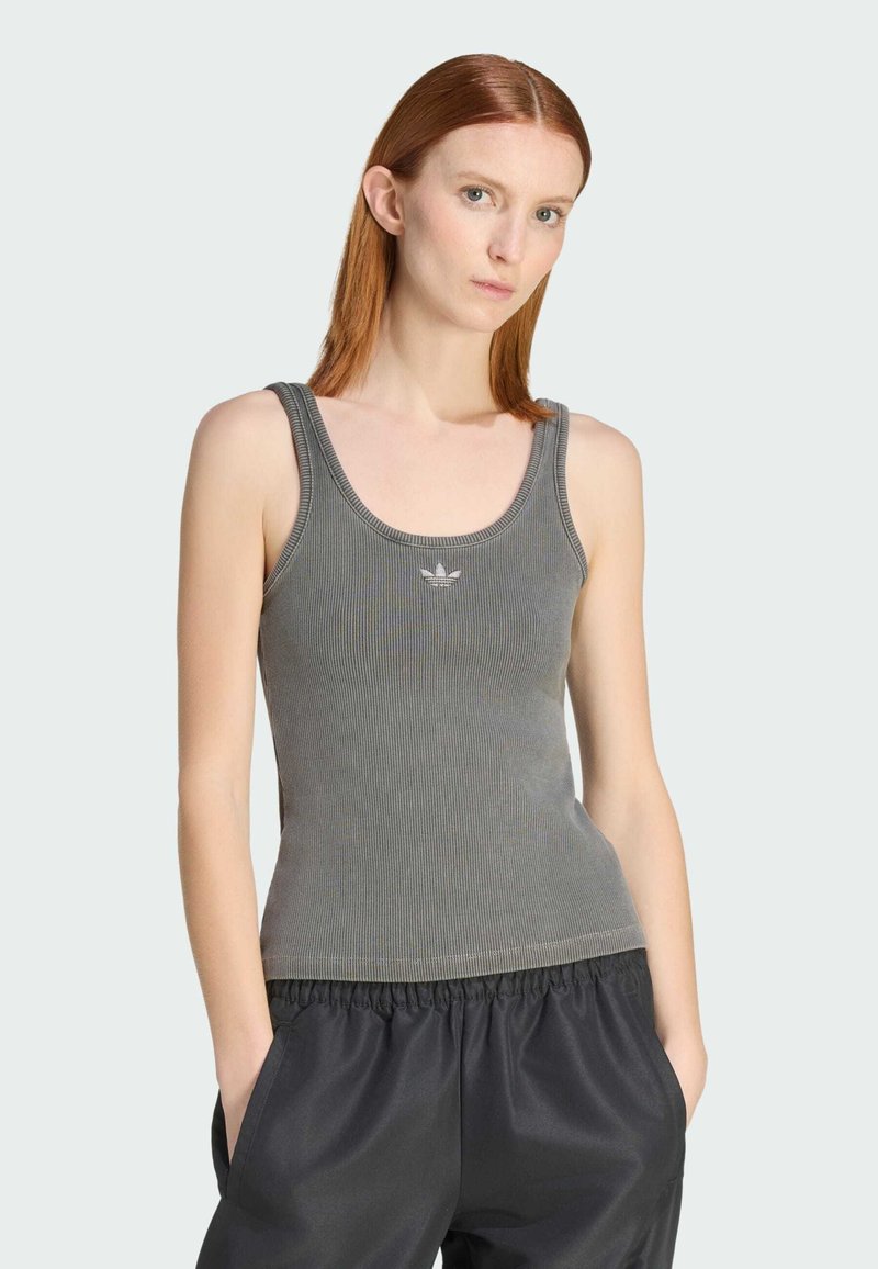 Camiseta sin mangas acanalada en gris oscuro con cuello redondo y tirantes finos, con un detalle sutil de logo en el pecho. Combinada con pantalones negros.