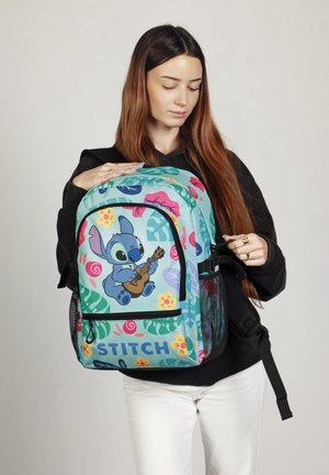 Mochila azul verdosa con estampados florales coloridos y el personaje Stitch. Cuenta con un bolsillo delantero con cremallera, bolsillos laterales de malla y correas ajustables.