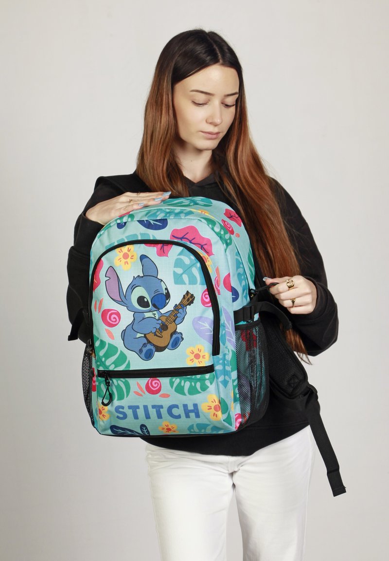 Sac à dos turquoise avec des imprimés floraux colorés et le personnage Stitch. Comprend une poche zippée à l'avant, des poches latérales en maille et des bretelles réglables.