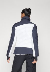 Padded Jacke mit hohem Kragen, die ein Farbschema in Marineblau und Weiß präsentiert. Strukturiertes Material mit eleganten Linien und engen Ärmeln.