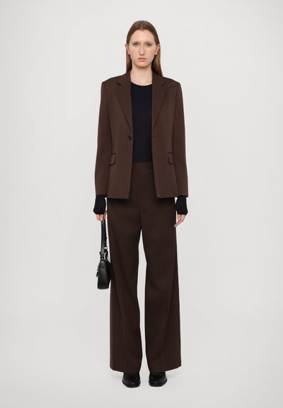 Brown suit featuring a tailored blazer with notch lapels, wide-leg trousers, and a fitted black top; held a small black bag.