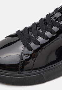 Schwarze Lacklederschuhe mit strukturierten schwarzen Schnürsenkeln, glatter Außenseite, runder Zehenform und einer Gummisohle mit einem dezenten Profilmuster.