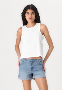 Vit ärmlös topp med hålmönster, rund halsringning; kombinerad med ljusblå denimshorts med uppvikt fåll och framfickor.