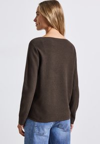 Maglione marrone a coste con scollo ampio, maniche lunghe e vestibilità rilassata, abbinato a jeans in denim azzurro chiaro.