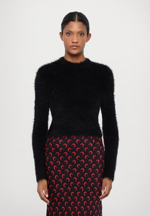 Black fuzzy sweater with long sleeves and a round neckline, paired with a patterned skirt featuring red crescent shapes on a black background.
