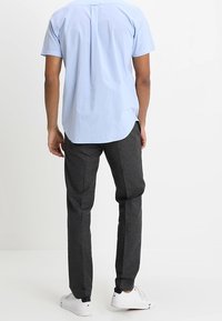 Niebieska koszula z krótkim rękawem z plisą z tyłu, połączona z ciemnoszarymi zwężanymi spodniami z pionowymi paskami i elastycznymi mankietami. Białe sneakersy.