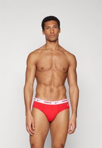 Rdeče bombažne spodnjice z belim elastičnim pasom, na katerem je logotip Nike. Dizajn je tesno prilegajoč, poudarja obliko telesa.