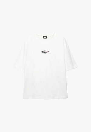 Fehér pamut póló rövid ujjakkal és kerek nyakkivágással, a mellkasán egy kis hímzett napszemüveg grafikával.