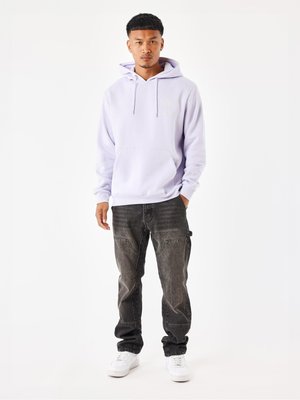 Hoodie de lavanda claro con un bolsillo frontal, combinado con jeans negros desgastados. Zapatillas blancas completan el conjunto. Diseño minimalista con cordones.