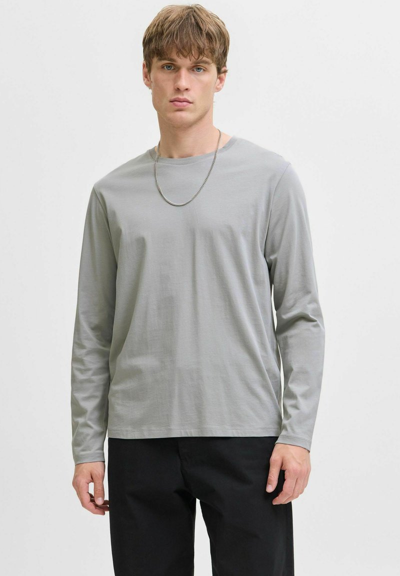 Grijze longsleeve shirt van zachte stof, met een ronde halslijn en een ontspannen pasvorm, gecombineerd met zwarte broek.