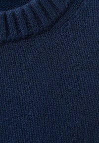 Temno modra pletena tkanina puloverja s rebrastim ovratnikom, teksturirano pletenjem in mehkim zaključkom. Površina prikazuje subtilne razlike v debelini.