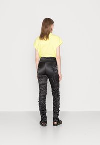 Top amarelo de mangas curtas combinado com calças pretas de cintura alta e pregas, apresentando uma textura suave e sandálias pretas planas. Design minimalista.