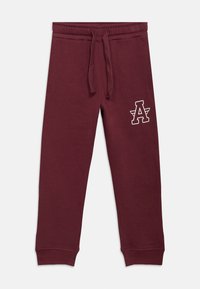 Μπορντό φόρμα με ελαστική μέση και κορδόνι, με λευκό λογότυπο "A" στο αριστερό ισχίο και ριμπ μανσέτες στους αστραγάλους.