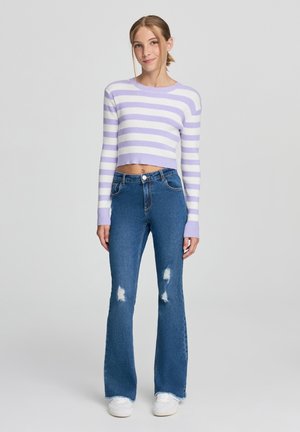 Maglione corto a righe viola chiaro e bianco abbinato a jeans a zampa d'elefante blu con dettagli di strappi alle ginocchia e sneakers bianche.