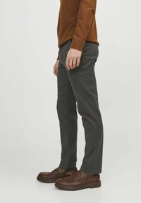Graue Hose mit maßgeschneidertem Schnitt und glatter Textur, kombiniert mit braunen Slippern und einem rostfarbenen Pullover. Die Seitenansicht zeigt klare Linien.
