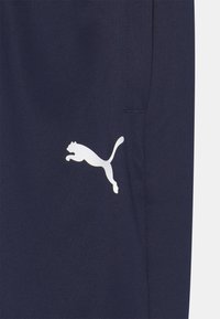 Marinefarbene Sporthosen aus strukturiertem Material, mit einem weißen springenden Puma-Logo an Oberschenkel und einer Seitenstasche.
