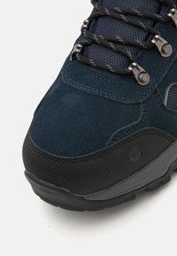 Zapato de senderismo de ante y malla azul oscuro con acentos negros; presenta ojales metálicos y suela texturizada para tracción. Vista en primer plano de la puntera.