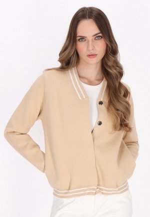 Beige gebreide cardigan met een V-hals, voorzien van twee zwarte knopen en witte strepen langs de kraag en zoom. Soepele textuur.