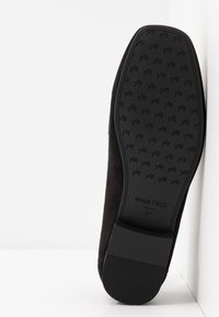 Chaussure en daim noir avec une semelle plate, dotée d'une semelle en caoutchouc texturée et d'un logo de marque en relief. Taille 37 indiquée sur la semelle.