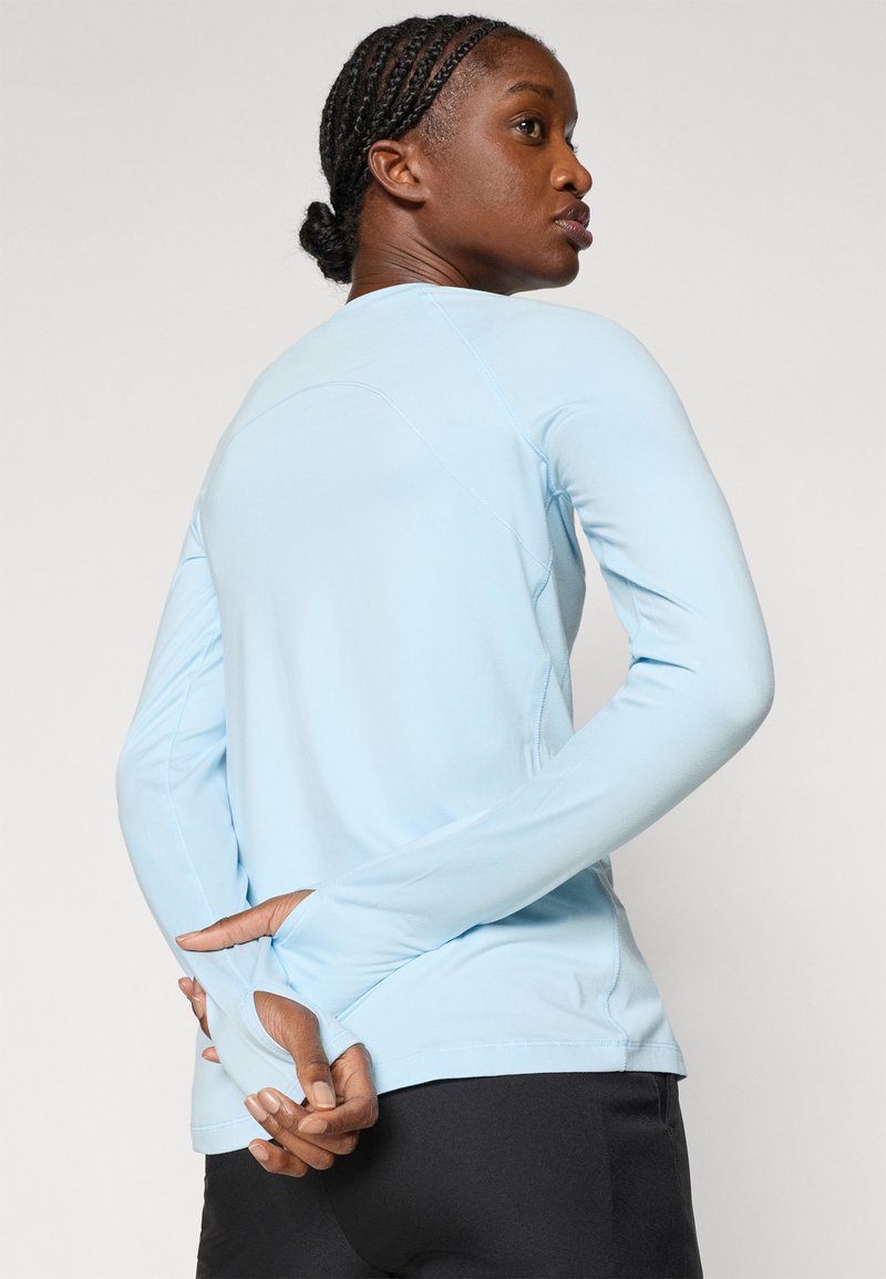 Jasnoniebieska, długorękawowa koszulka sportowa z otworami na kciuki, o dopasowanym kroju i gładkiej fakturze. Widoczne detale szwów na plecach i rękawach.