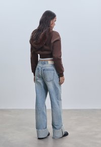 Smešani smeđi skraćeni dukserica s kapuljačom obloženom umjetnim krznom, uparen s svijetloplavim širokim trapericama s poderanim rubovima i klasičnom traper teksturom.