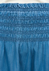 Μπλε τζιν ύφασμα με πολλαπλές σειρές σφιχτής, μαζεμένης ελαστικής πλέξης που δημιουργεί υφή ρυτιδωμένου υφάσματος και ραμμένες οριζόντιες γραμμές.