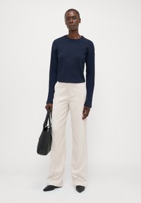Pull en maille bleu marine avec un design texturé, associé à un pantalon en velours côtelé large couleur crème. Sac à main noir et chaussures à bout pointu en vedette.